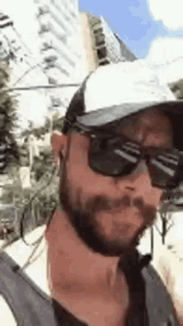 a man with a beard and sunglasses is wearing a hat and tie .