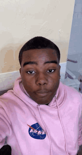 a young man wearing a pink nasa sweatshirt takes a selfie