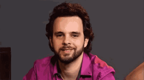 a man with a beard is wearing a purple shirt and smiling .