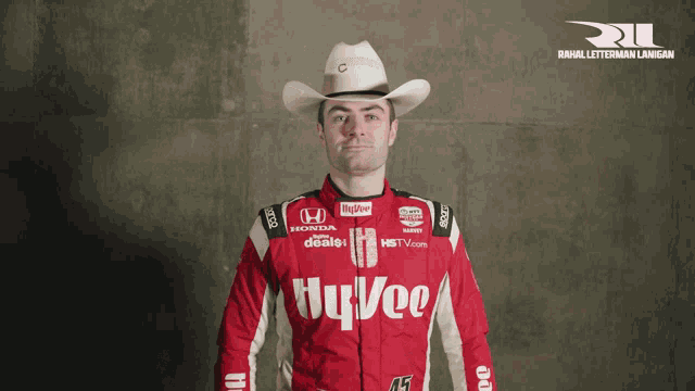 a man in a cowboy hat is wearing a red hy vee jacket