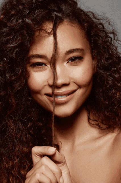 a woman with curly hair is smiling while holding a piece of her hair