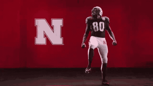 a football player is dancing in front of a red background with the letter n .