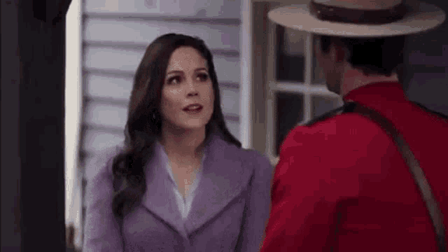 a woman in a purple coat is talking to a man in a red hat .