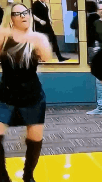 a woman wearing glasses and knee high boots is standing in front of a mirror