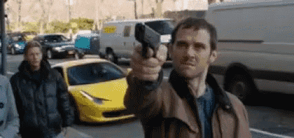 a man is holding a gun in front of a yellow sports car .