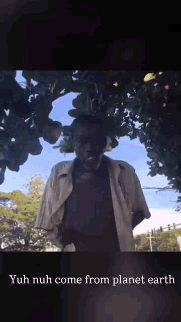 a man is standing under a tree with the words yuh nuh come from planet earth below him