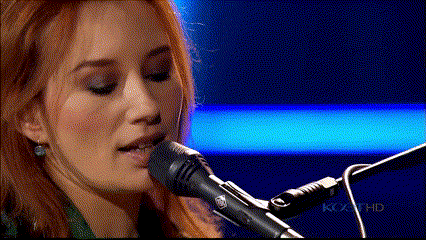 a close up of a woman singing into a microphone with a blue background
