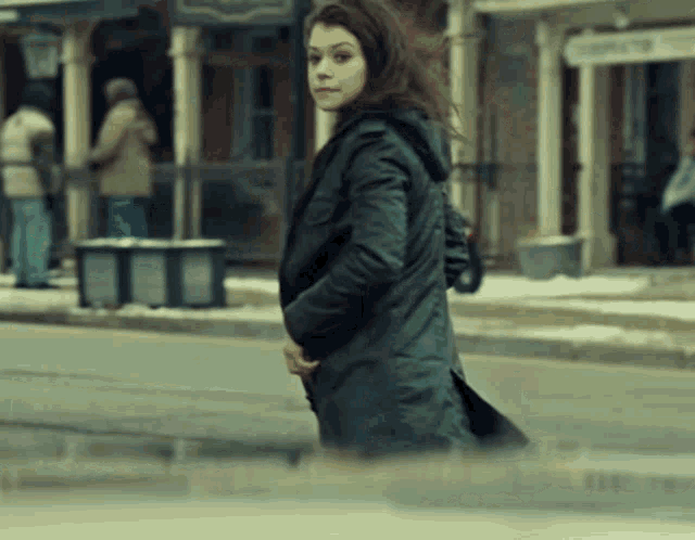 a woman in a black coat is walking down a snowy street