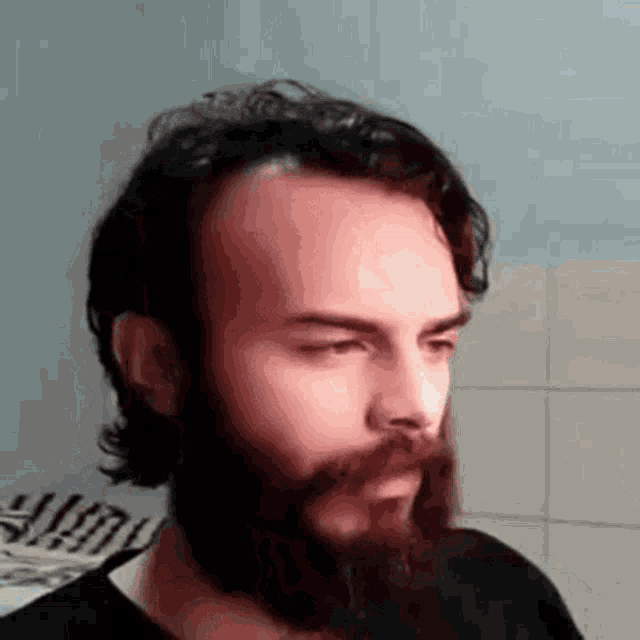 a man with a beard and long hair is wearing a black shirt and looking at the camera .