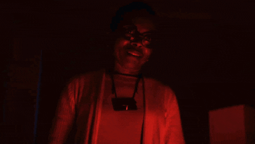 a woman wearing glasses is standing in a dark room and smiling