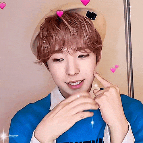 a young man wearing a beret and a blue sweater is making a heart shape with his finger .