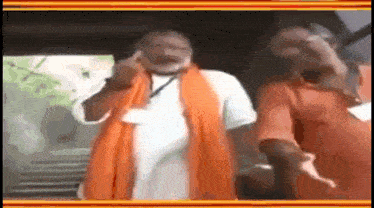 a man in an orange scarf is giving a middle finger while standing next to another man .