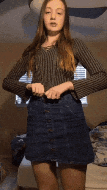 a girl wearing a sweater and a denim skirt is standing in a bedroom