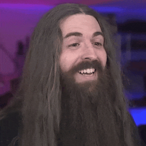 a man with long hair and a beard is smiling with his mouth open .