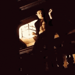 a man without a shirt is standing in a dark room with his arms in the air .