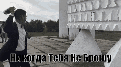 a man in a suit is holding a bottle in front of a statue with russian writing on it .