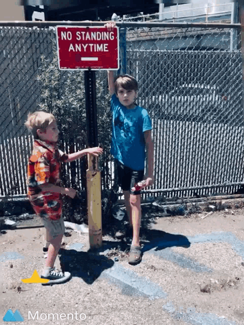 two young boys are standing in front of a no standing anytime sign