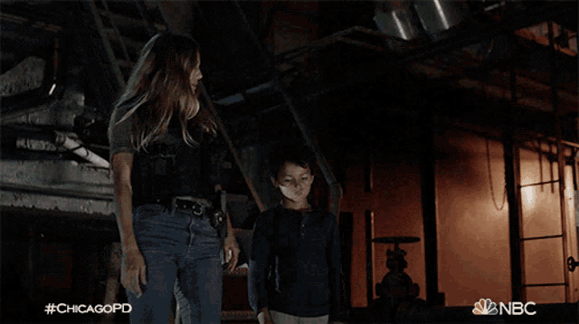 a woman and a boy are walking in a dark room with nbc written on the bottom