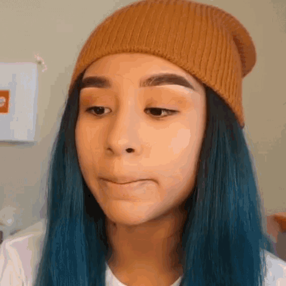 a girl with blue hair and a beanie is making a face .