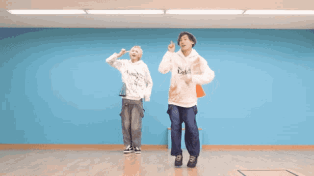 two people are dancing in a room with a blue wall and one has a hoodie that says ' a ' on it