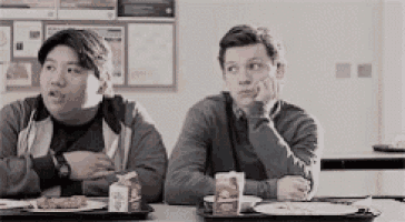 two young men are sitting at a table with a tray of food in a cafeteria .