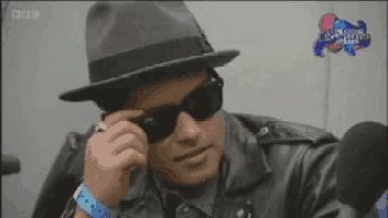 a man wearing a hat and sunglasses is sitting in front of a microphone with the words big world on the screen behind him