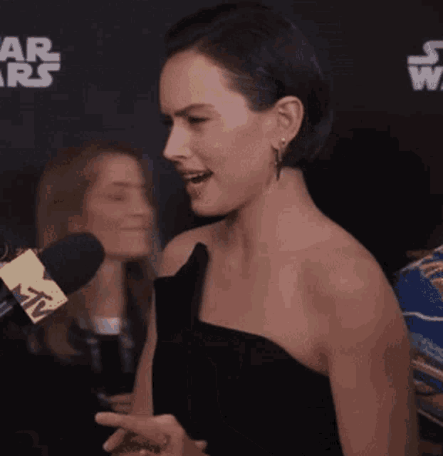 a woman in a black dress is talking into a microphone with a star wars logo in the background