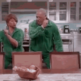 a man and a woman are dancing in a kitchen while wearing green jumpsuits .