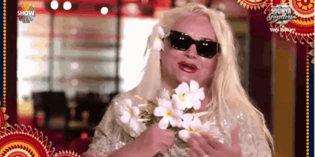 a woman wearing sunglasses is holding a bunch of white flowers .