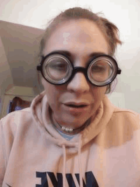 a woman wearing glasses and a sweatshirt is making a funny face .