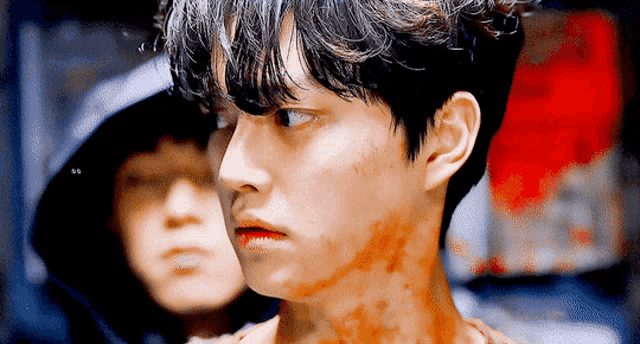 a young man with blood on his face is looking at the camera