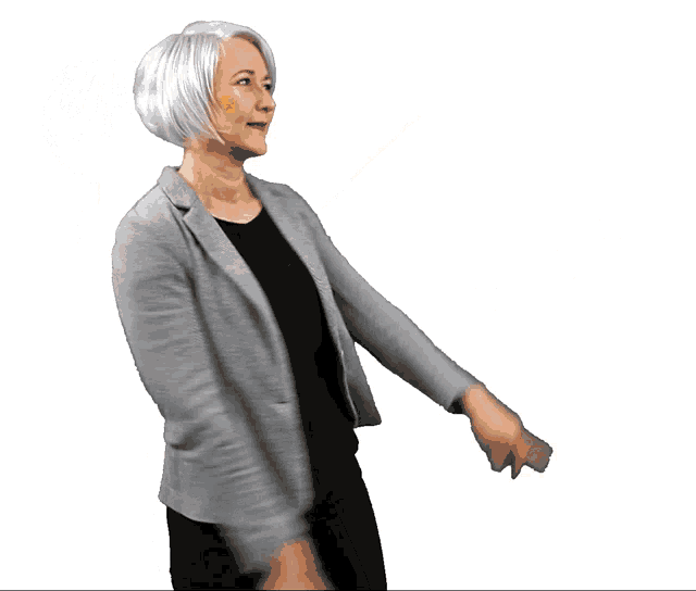 a woman wearing a grey jacket and black pants is pointing her fingers