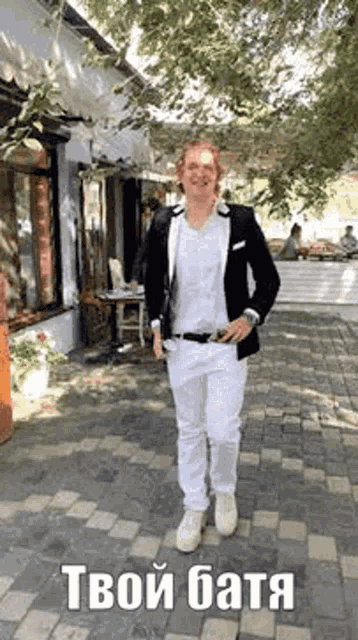 a man in a black jacket and white pants is walking down a brick sidewalk .