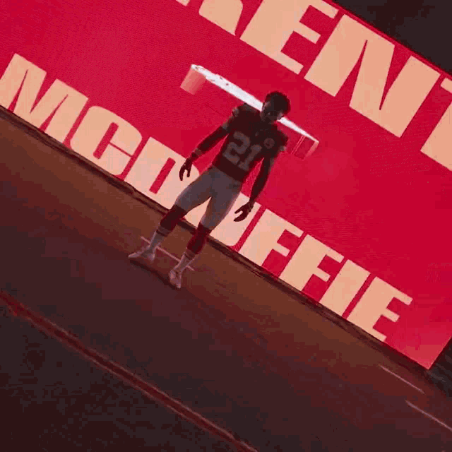 a football player wearing number 21 stands in front of a large red sign