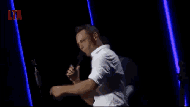 a man in a white shirt is singing into a microphone on a stage .