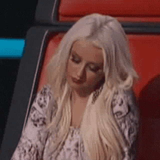 a woman with blonde hair is sitting in a red chair and looking down .