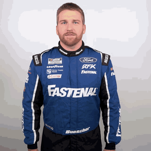 a man wearing a blue fastenal jacket stands in front of a white wall