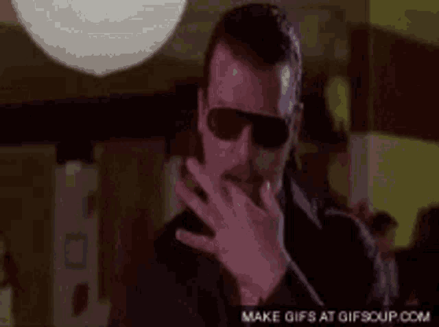 a man is wearing sunglasses and covering his mouth with his hand .