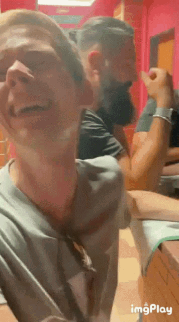 a man with a beard is laughing while another man watches