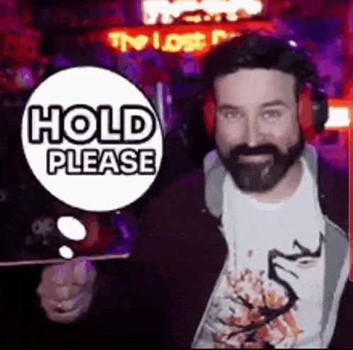 a man with a beard wearing headphones is holding a sign that says `` hold please '' .