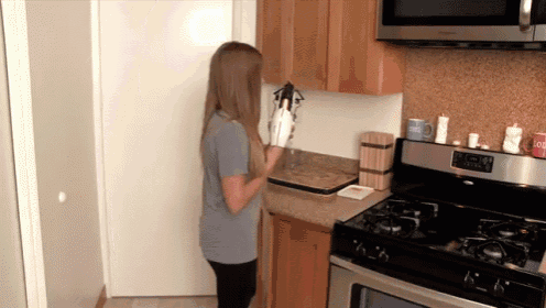a woman standing in a kitchen with a stove and a cup that says " soup " on it