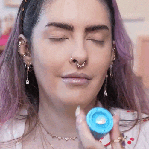 a woman with purple hair and a nose ring has her eyes closed and is holding a blue object