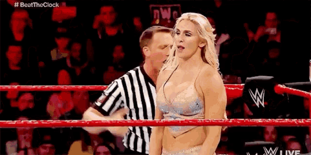 a woman in a wrestling ring with a referee standing behind her .