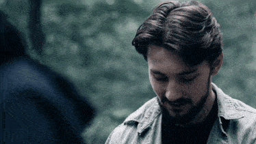 a man with a beard wearing a grey shirt looks down