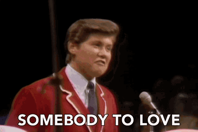 a man singing into a microphone with the words " somebody to love " behind him