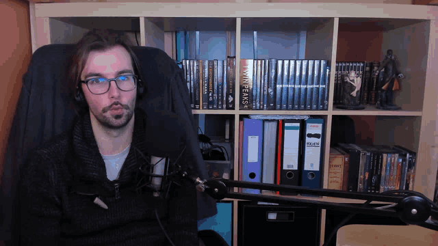 a man wearing headphones sits in front of a bookshelf with a book called twin peaks on it