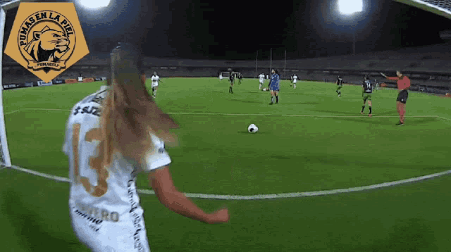 a woman in a pumas en la ribera jersey kicks a soccer ball on a field