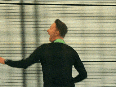 a man in a black sweater is standing in front of a striped wall with his mouth open