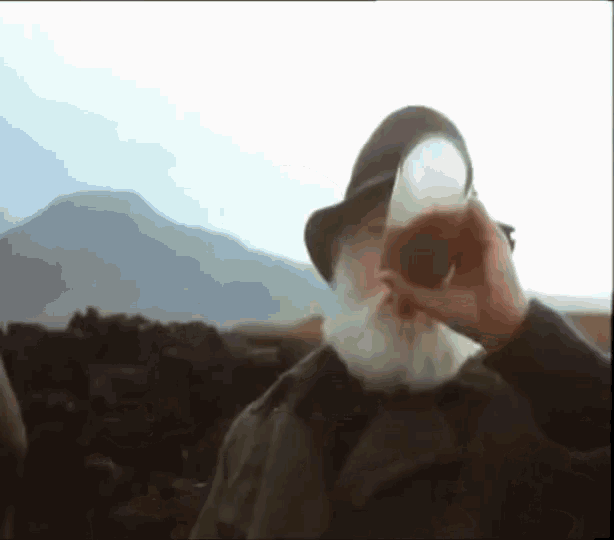 a man with a beard is drinking from a cup with mountains in the background