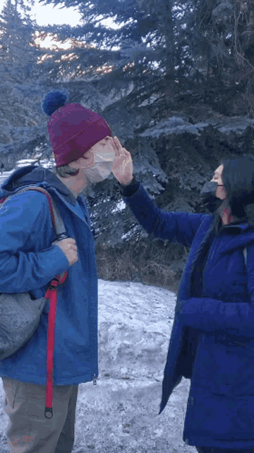 a person wearing a mask reaches out to touch another person 's nose
